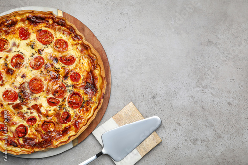 Delicious homemade prosciutto quiche and spatula on light gray table  flat lay. Space for text