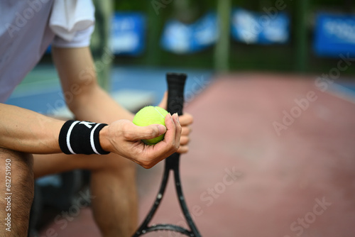 Select focus on hands of male tennis player holding ball racket sitting on the bench at tennis court