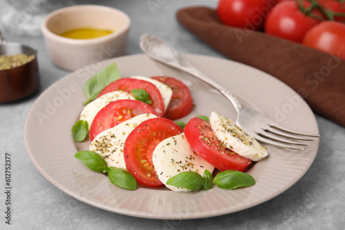 Delicious Caprese salad with tomatoes, mozzarella, basil and spices on light grey table, closeup