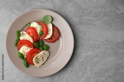 Delicious Caprese salad with tomatoes, mozzarella, basil and spices on light grey table, top view. Space for text