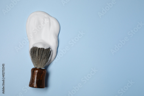 Brush with shaving foam on light blue background, top view. Space for text
