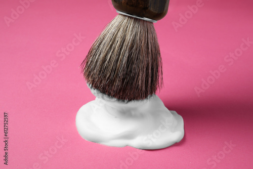 Dipping brush into shaving foam on pink background, closeup