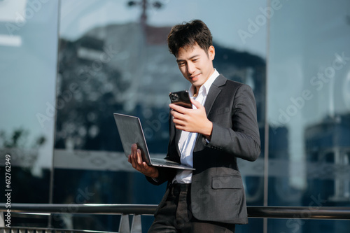 Young Asian business man working at outside business center with laptop, tablet, smartphone and taking notes on the paper.