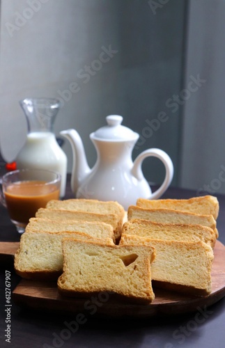 Tea Time Snack. Healthy Wheat rusk served with Indian hot masala tea and milk jug over black background. also known as Mumbai cutting chai. with Copy space. Crunchy rusk or toast.