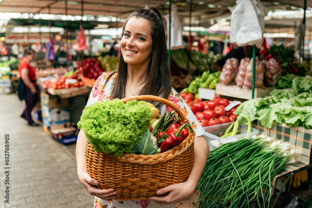  portrait of a smiling Caucasian girl holding a basket filled with fruits and vegetables she bought at the market.