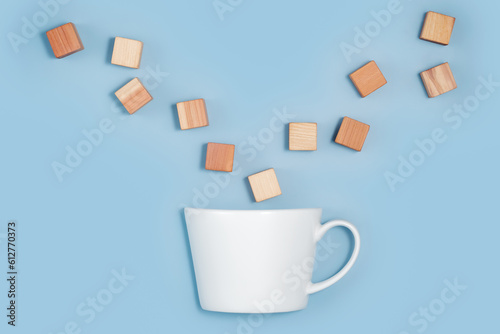 blank wooden cubes falling into a white cup on blue background. Minimalistic abstract concept representation of building creating and diversity. Top view flat lay copy space