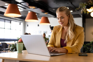 Happy plus size caucasian casual businesswoman using laptop at desk