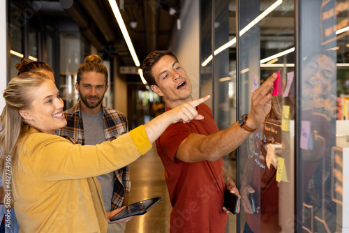 Happy diverse creative colleagues in discussion brainstorming making notes on glass wall in office