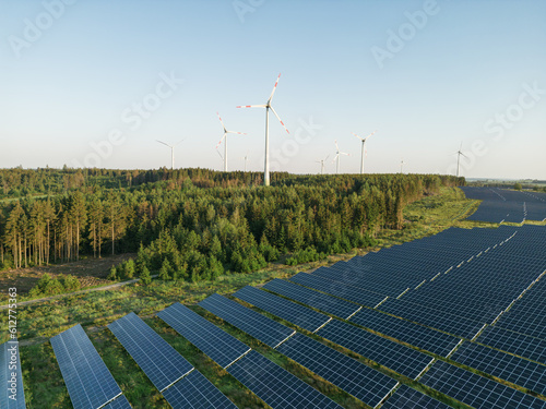 Photovoltaik-Anlage in grüner Landschaft mit Windrädern im Hintergrund bei Sonnenschein photo