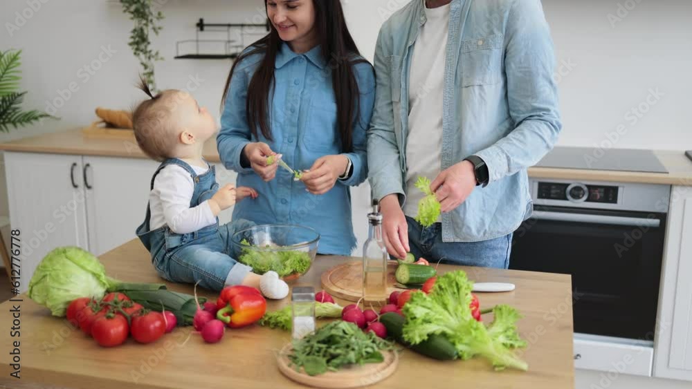 Sweet little girl in denim wear holding small slice of red vegetable while caring mother describing new product. Mother and daughter getting to know more about texture and color of hard food. Sweet little girl in denim wear holding small slice of red vegetable while caring mother describing new product. Mother and daughter getting to know more about texture and color of hard food.