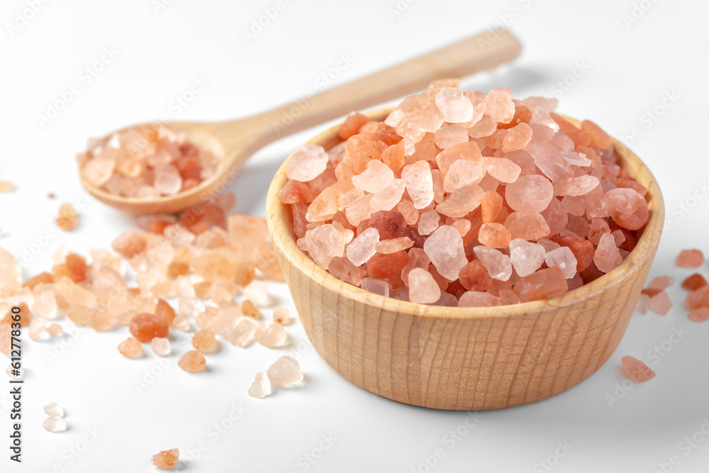 Himalayan pink salt in wooden bowl with spoon on white background Himalayan pink salt in wooden bowl with spoon on white background