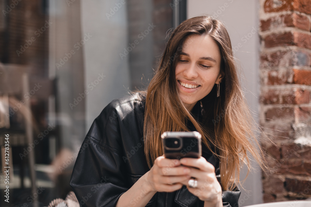 Portrait of happy female dressed casually holding mobile phone, typing messages, communicating with friends via social networks, using high Internet connection at cafe. Woman look flirting.