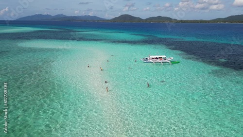 Tourists swim in clear blue water of balabac palawan on sand bar by banca boat photo