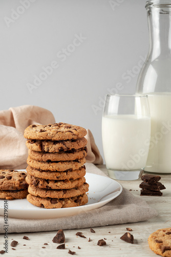 Stack of chocolate chip cookies and glass of milk on white wooden table