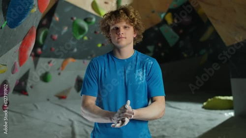 Portrait of a young man climber, guy stands against the background of a climbing wall and use magnesia before climbing. photo