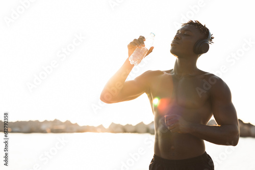 Fitness training outdoors. Handsome African man preparing for the training. Thirsty athlete drinking water.