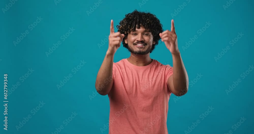 young indian man pointing index finger on camera standing isolated over blue studio background young indian man pointing index finger on camera standing isolated over blue studio background