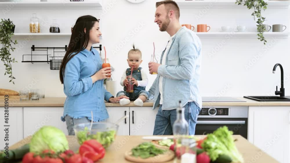 Delightful parents and kid enjoying refreshing glass of fresh juice while creating meal in modern kitchen. Mom and dad adorably gazing at cute daughter. Family spending quality time together at home. Delightful parents and kid enjoying refreshing glass of fresh juice while creating meal in modern kitchen. Mom and dad adorably gazing at cute daughter. Family spending quality time together at home.