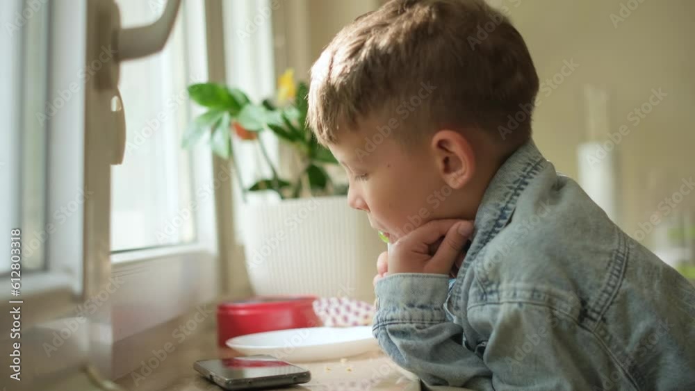 A boy eats a sandwich or a bun and looks at the phone. A boy eats a sandwich or a bun and looks at the phone.