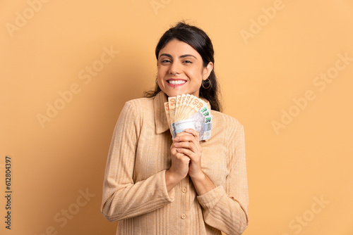 cheerful young woman showing money, brazilian currency in all beige colors. business, loan, pay, wealth concept. 