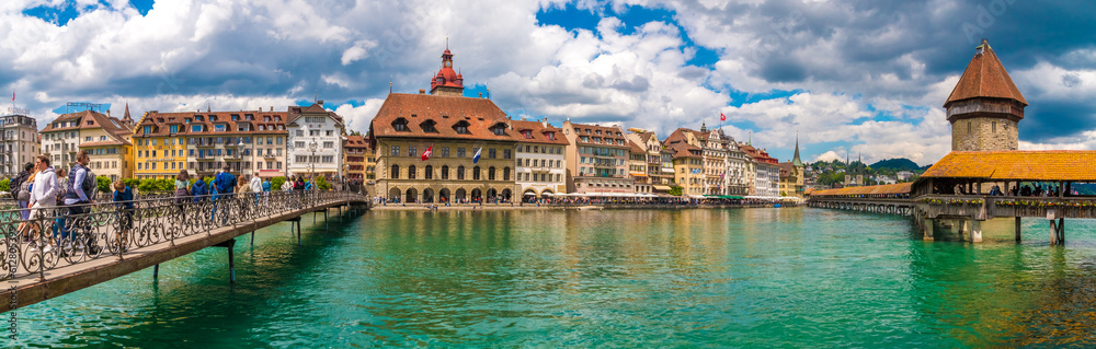 Lovely huge panorama picture of Lucerne's old town boulevard along the river Reuss with people on the bridge Rathaussteg and the famous Kapellbrücke (Chapel Bridge).