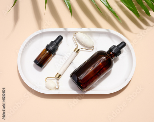 Glass bottles with a pipette  a stone face massager on a white plate  top view