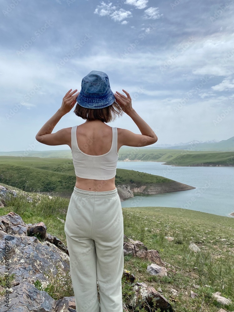 A slender 30-year-old girl with short hair, sportswear and a panama hat, looks at the lake. Relaxation, recreation, tourism, travel