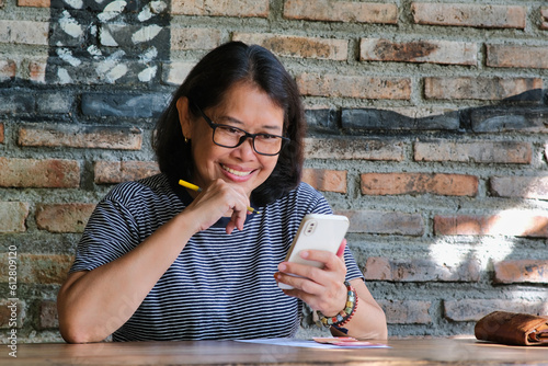 A middle-aged woman smiling cheerfully while looking at her smartphone photo
