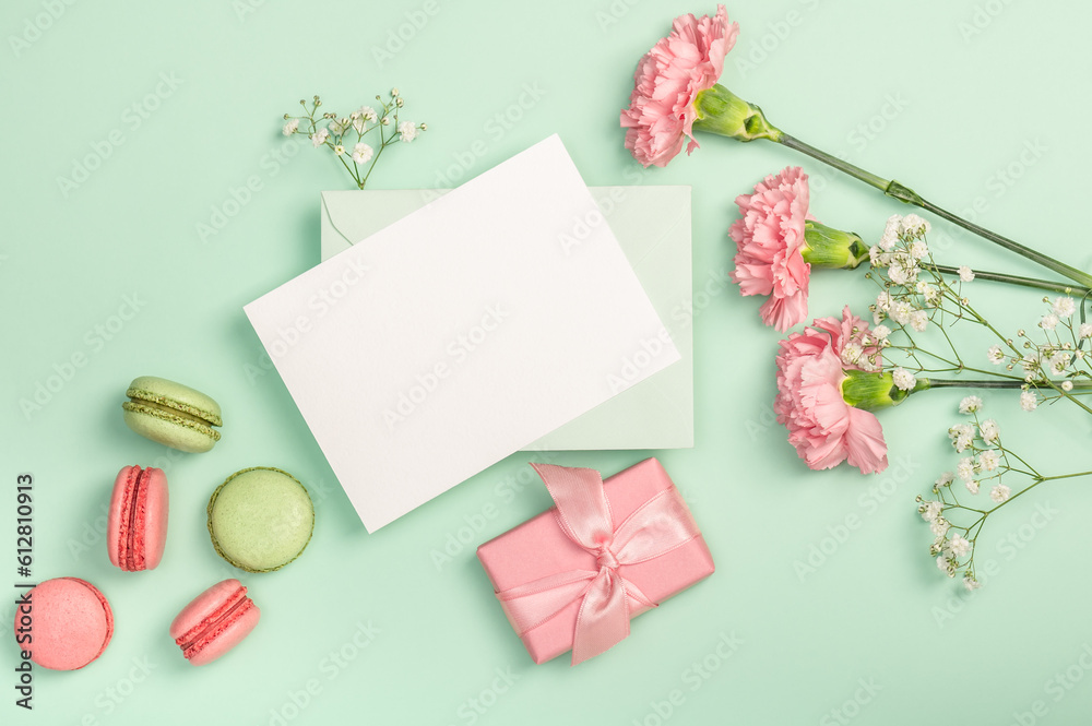 Flat lay composition with empty blank, gypsophila, pink carnations and macaroons on a light green background. Postcard.
