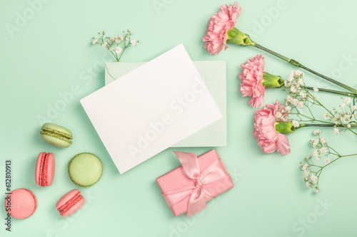 Flat lay composition with empty blank, gypsophila, pink carnations and macaroons on a light green background. Postcard.