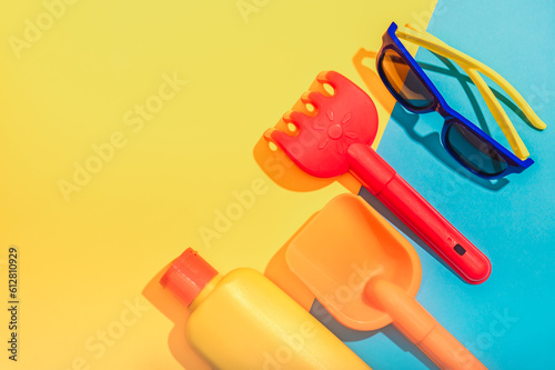 A tube of sunscreen, sunglasses and children's beach toys on a blue and yellow background. Sun protection . © Natalia