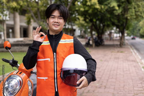 Canvas Print Happy young Thai motorcycle taxi driver or rider waiting for passenger near by the building in the city