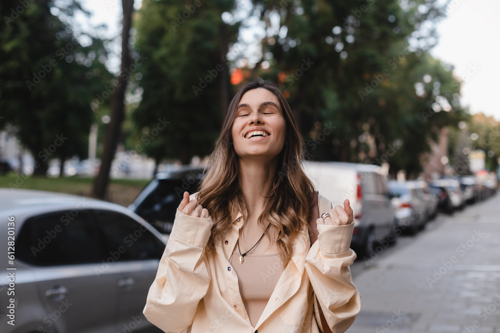 Fototapeta premium Young excited confident proud blonde woman winner wearing yellow shirt on street, raising hands, feeling power, motivation, energy, celebrating career, traveling success in big city outdoors.