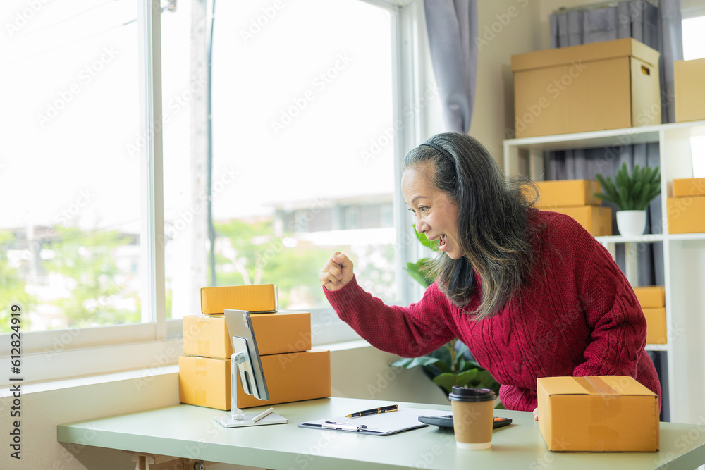 Successful old businesswoman smiling happily receiving new buzzer Asian woman owns a small business online with shipping boxes. concept of working at home Successful old businesswoman smiling happily receiving new buzzer Asian woman owns a small business online with shipping boxes. concept of working at home
