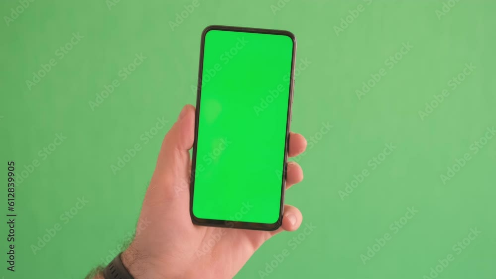Man's hand holding a black smartphone with green screen slide up and slide down display, Man using mobile phone with chroma key touch display on green background.