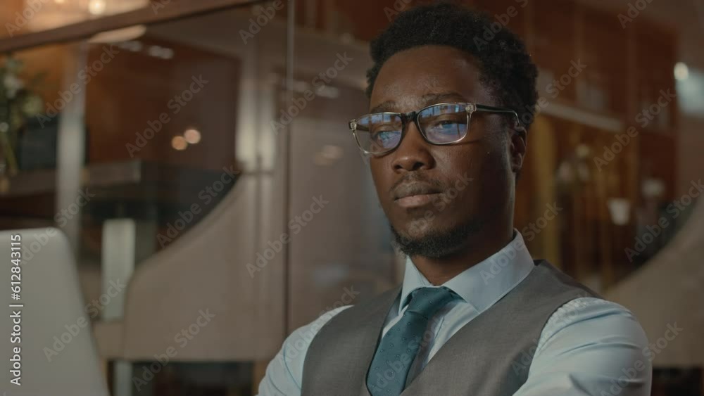 Chest up of successful young Black man in elegant formalwear working on laptop with screen reflecting in his eyeglasses