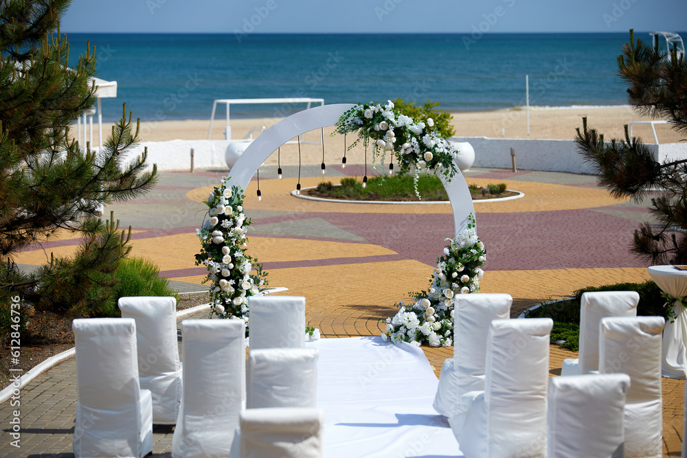 White wedding arch with white roses on the seashore