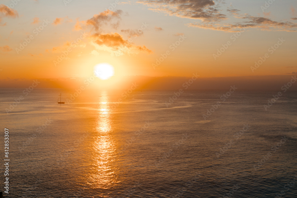 Sunset against the backdrop of the ocean and yacht. Beautiful yellow sun sets over the sea