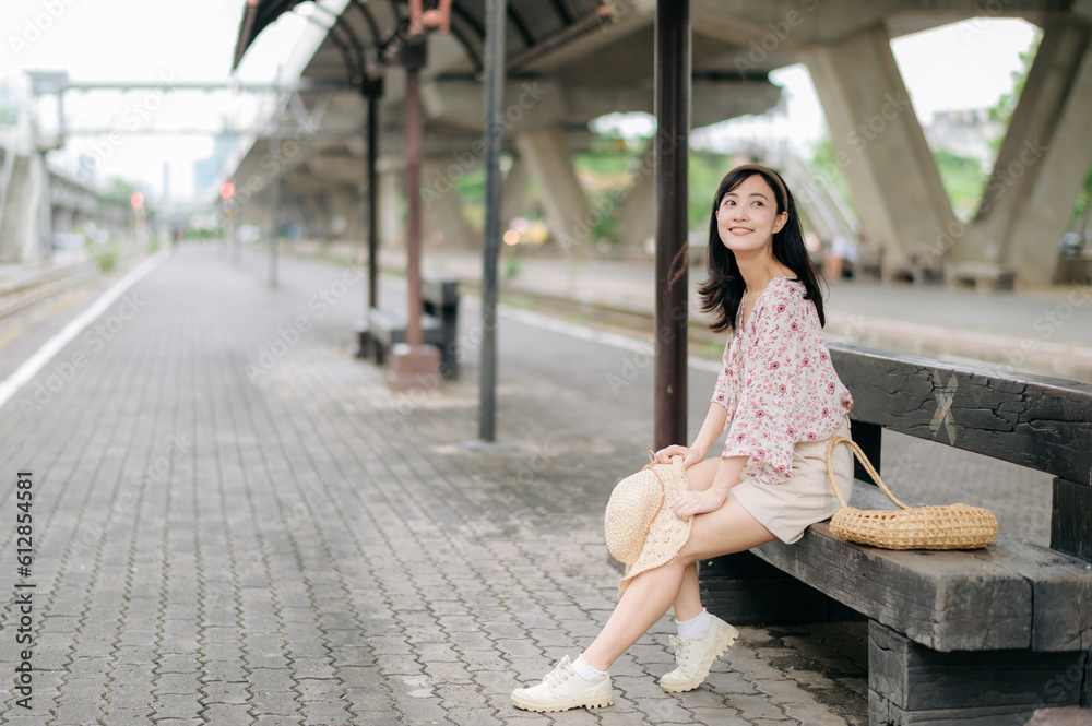 Fototapeta premium young asian woman traveler with weaving basket waiting for train in train station. Journey trip lifestyle, world travel explorer or Asia summer tourism concept.
