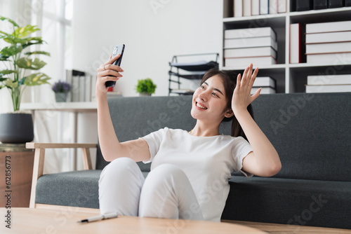 Pretty Asian woman sit on sofa at home enjoy with video call meeting with friend. Woman making content by smartphone at home
