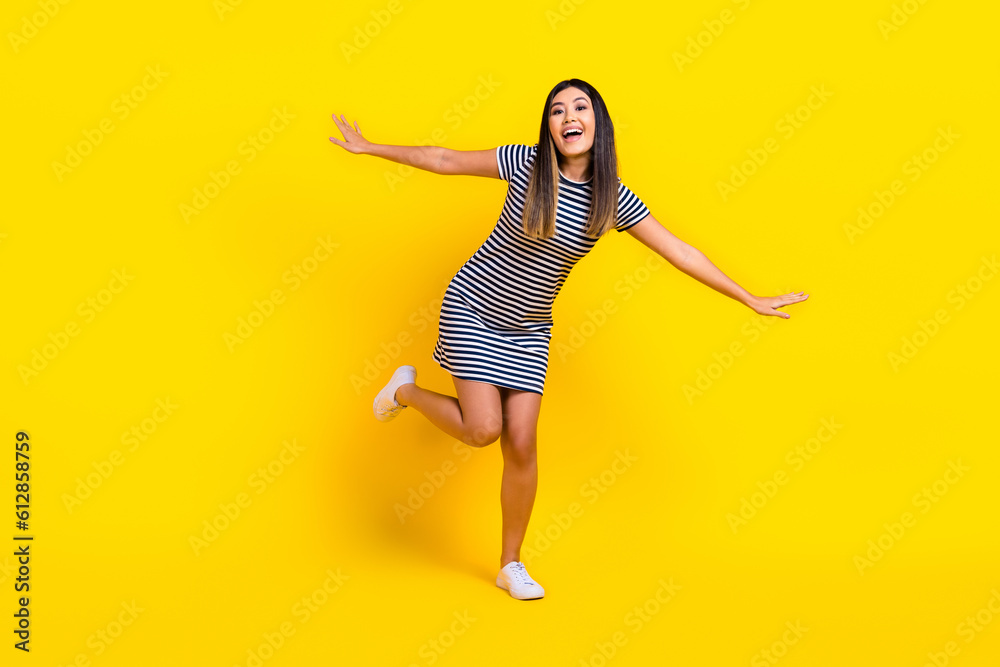 Full length photo of japanese girl wear striped dress have fun chill flying wings freedom party dance isolated on yellow color background Full length photo of japanese girl wear striped dress have fun chill flying wings freedom party dance isolated on yellow color background