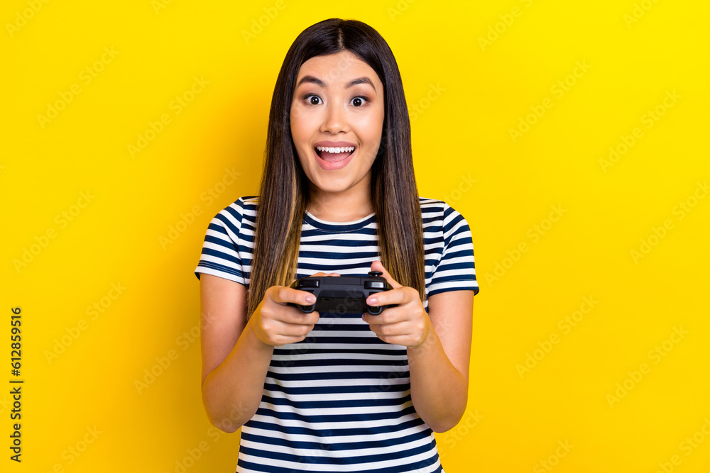Portrait of young chinese woman wear striped t-shirt hold gamepad addicted cyber player witcher 3 isolated on yellow color background Portrait of young chinese woman wear striped t-shirt hold gamepad addicted cyber player witcher 3 isolated on yellow color background