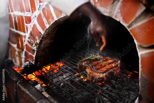 t-bone stake with rosemary grilling on chacoal cooking on a fire to make barbecue cusine in old style turnel at fire cooking kitchen photo