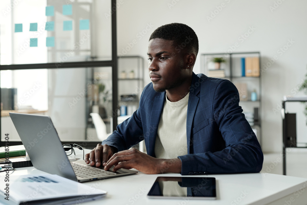 Young serious manager in elegant suit looking at laptop screen and analyzing online data or working over new business project Young serious manager in elegant suit looking at laptop screen and analyzing online data or working over new business project