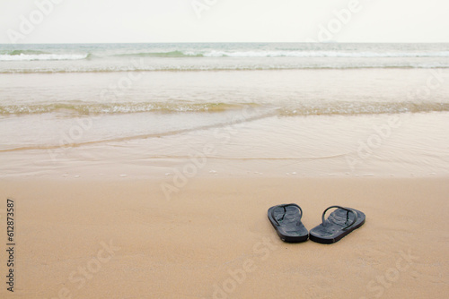 Black slippers feet at the beach, with a wave of foaming gentle beneath them.