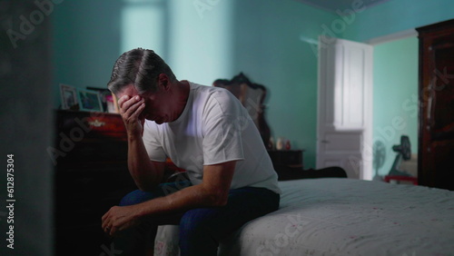 Depressed man sitting by bedside in bedroom. Sad unhappy person looking down suffering from mental illness © Marco