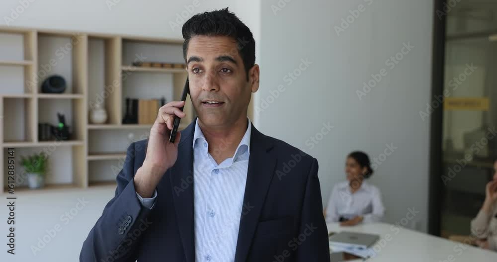 Indian businessman in formal suit lead conversation on cellphone standing in office board room solve business by phone call, talk to company client, provide information, help remotely, arrange meeting Indian businessman in formal suit lead conversation on cellphone standing in office board room solve business by phone call, talk to company client, provide information, help remotely, arrange meeting