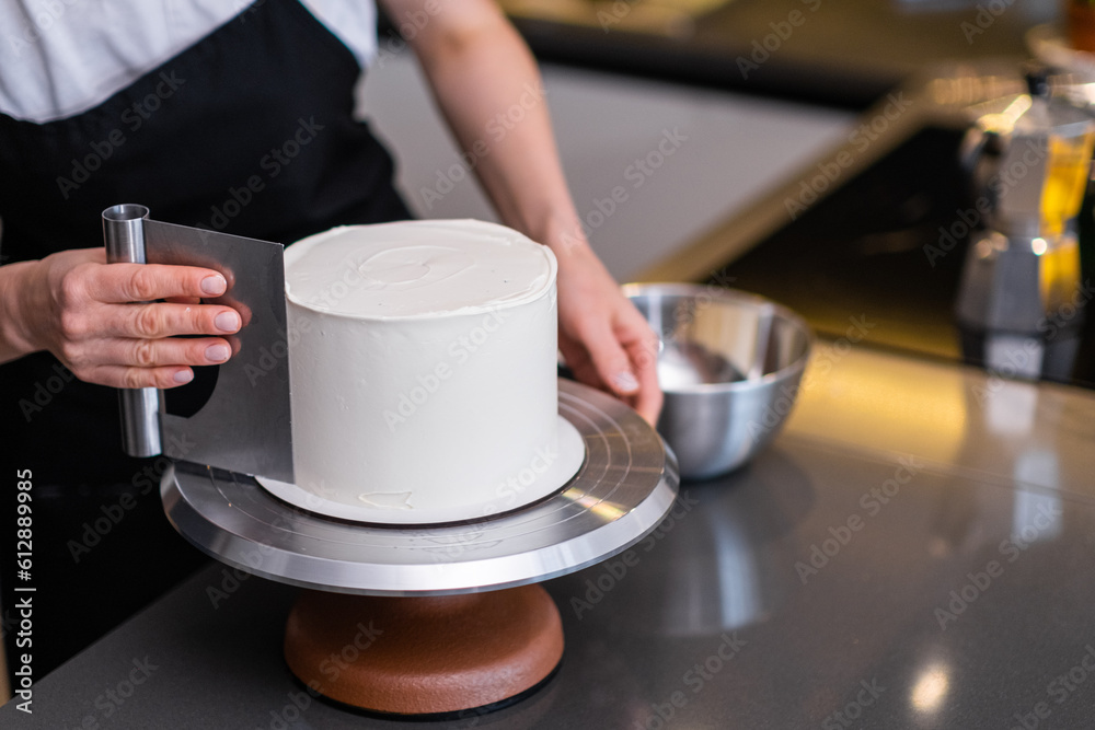 Professional confectioner handling white mastic on baked cake using metallic pastry scraper woman showing process of making custom confectionery from natural ingredients - obrazy, fototapety, plakaty 