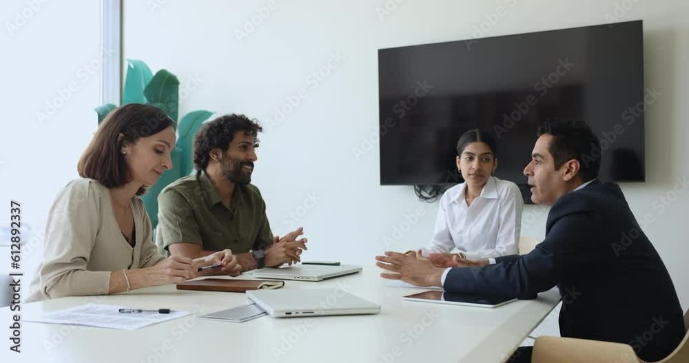 Four multiethnic business people negotiating, search solution, share ideas, discuss cooperation or contract details engaged in teamwork sit at desk in modern conference room. Briefing, meeting event