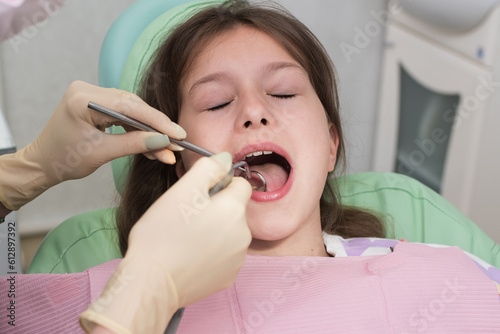 The hands of a pediatric dentist carry out the examination procedure of a smiling cute little girl sitting on a chair in the hospital. Dentist's office. A little girl is sitting in the dentist's 